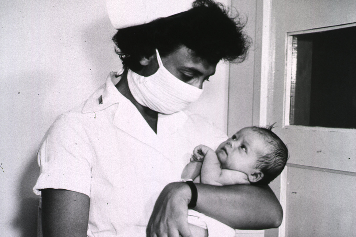 Historical image of a nurse wearing a mask and holding a baby in the 1940s