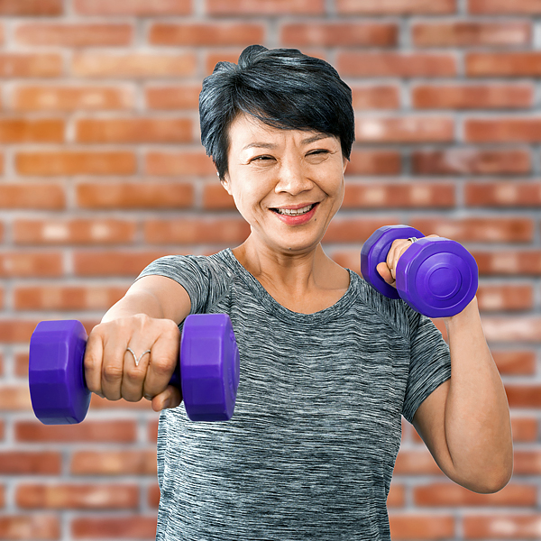 A senior woman working out with dumbbells in front of a brick wall