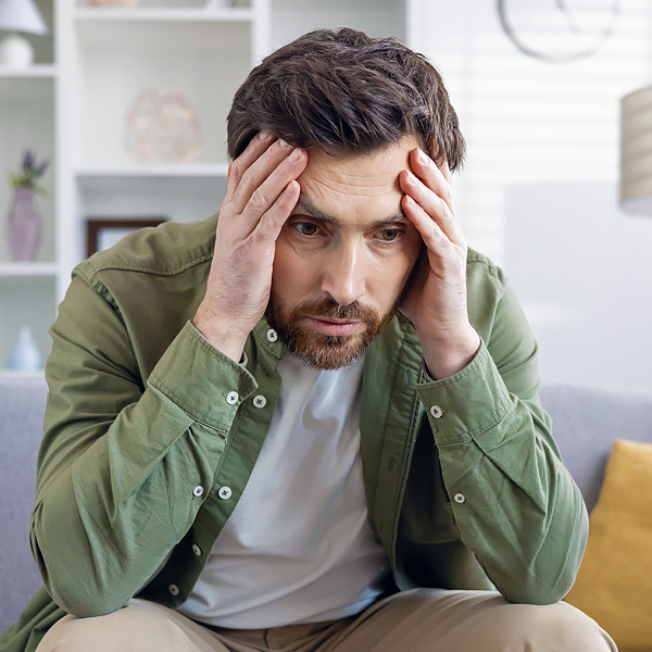 A man sitting on a couch and holding his head out of frustration