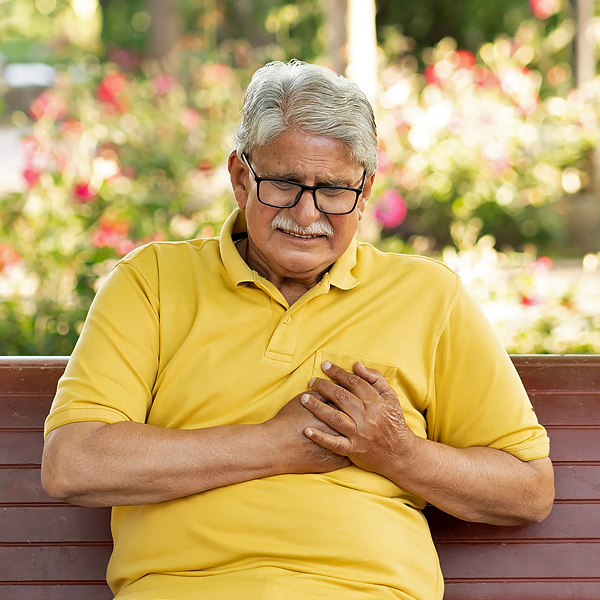 A senior man sitting on a park bench and holding his chest in pain