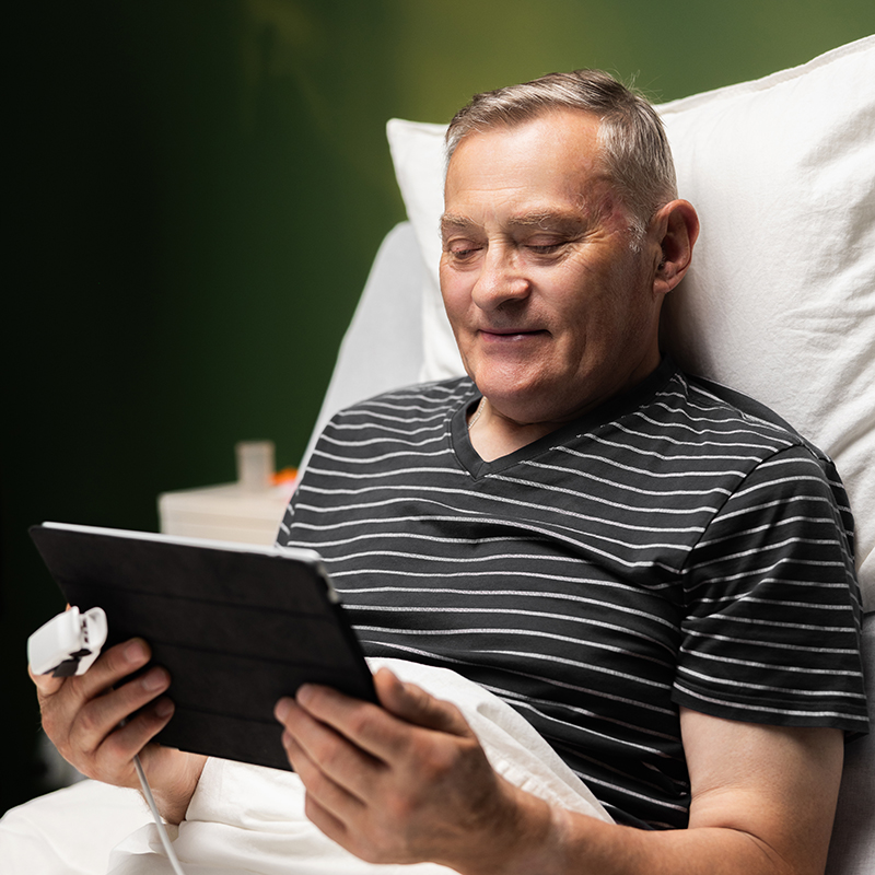 A man in a hospital bed looking at a computer tablet