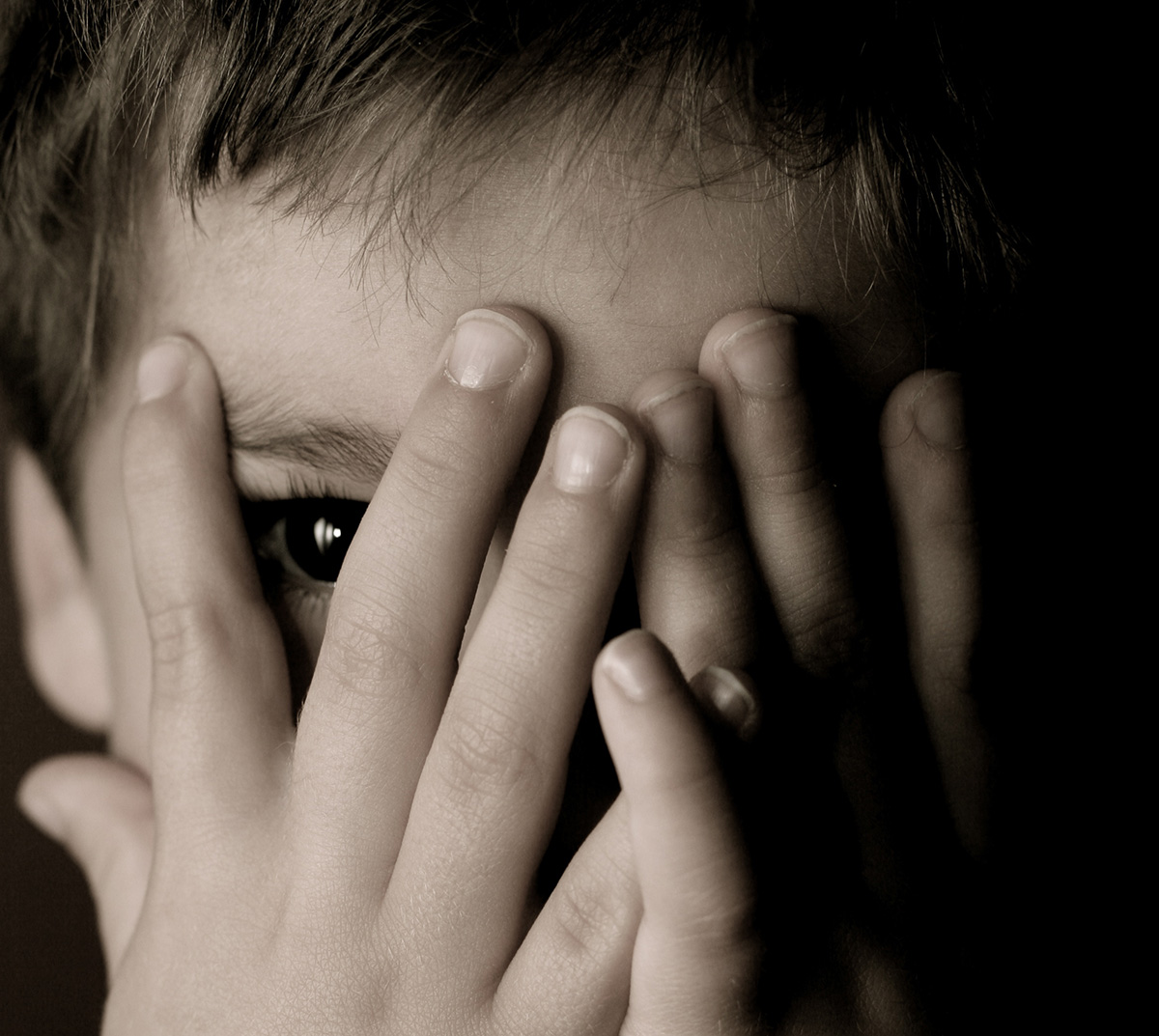 Child hiding face and looking through his fingers.