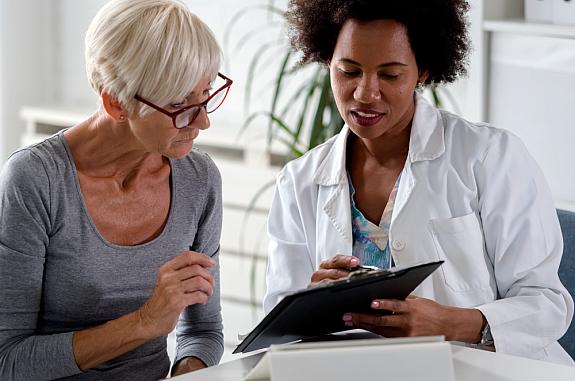 Female doctor speaking with an elderly female patient while looking at test results.