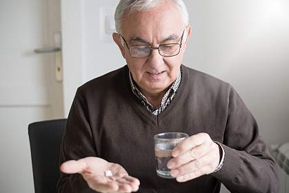 Elderly man looking at medicine and glass of water in his hands