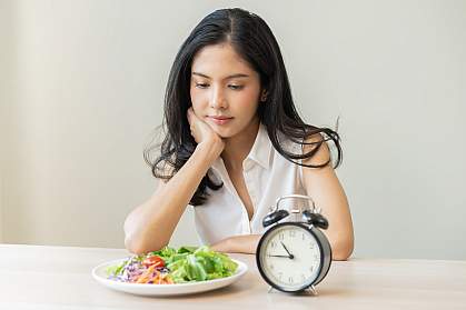 Young woman gazing at a salad beside an alarm clock showing 10:45.