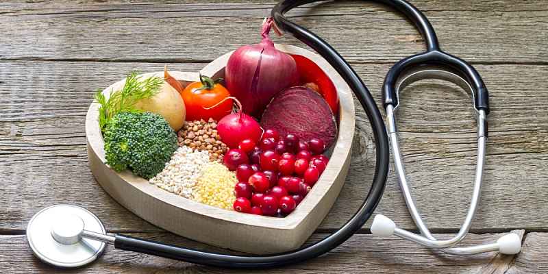 A heart shaped bowl filled with fruits and vegetables next to a stethoscope.