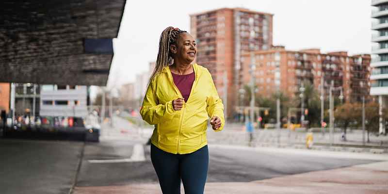 A middle-age African American woman with a yellow jacket walking briskly on the street.