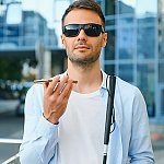A blind man with sunglasses on holding a cell phone and white cane