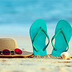 A sun hat, sunglasses, flip flops, and seashell on the beach