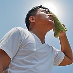 A man wiping sweat off his face with a towel while standing in the sun