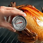 A close-up of someone measuring the temperature of a whole turkey with a meat thermometer