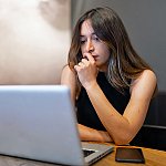 A pensive woman looking at a laptop