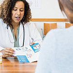 Medical practitioner sitting at her desk with a patient sharing a brochure while talking about prescription medication.