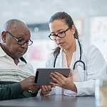 Image of a health care professional showing an older patient something on a tablet device.
