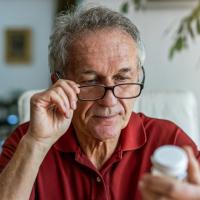An older man reading the label on a bottle of aspirin.