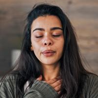 A woman with her eyes closed and hand on her chest, showing signs of anxiety.